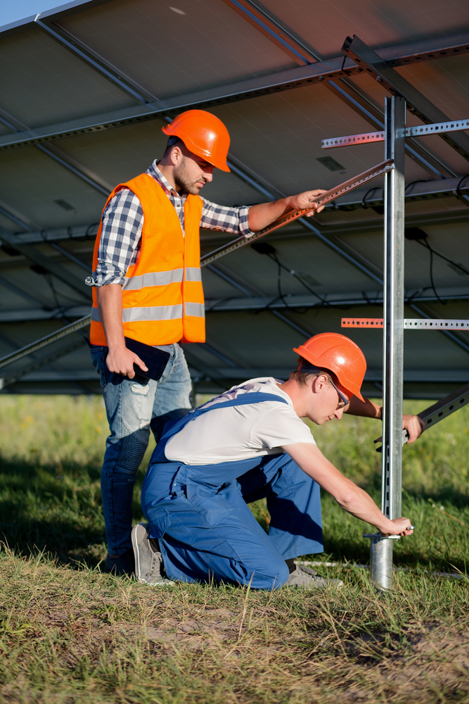 Builders installing frame with solar panels on helical pile. Engineers setting screw piles for solar power station.