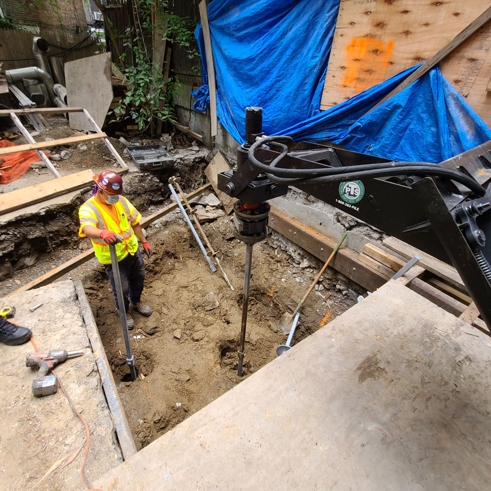 Crew member supervising drilling helical piles